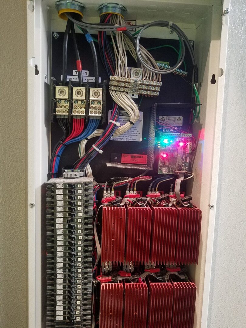 A white cabinet with many wires and some red batteries