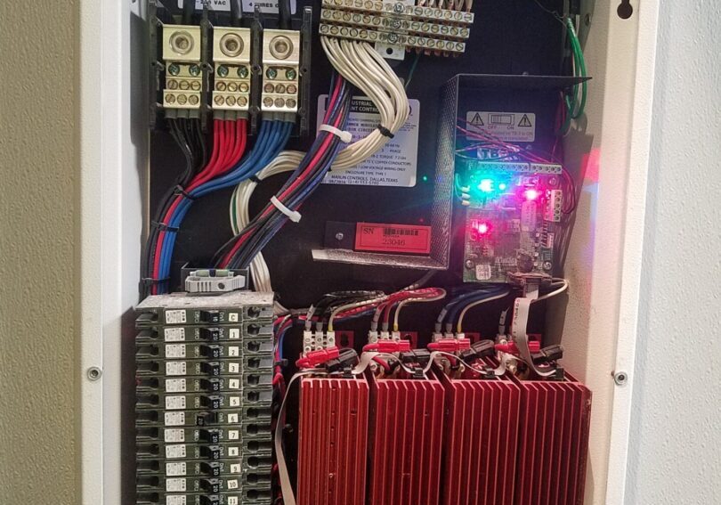 A white cabinet with many wires and some red batteries